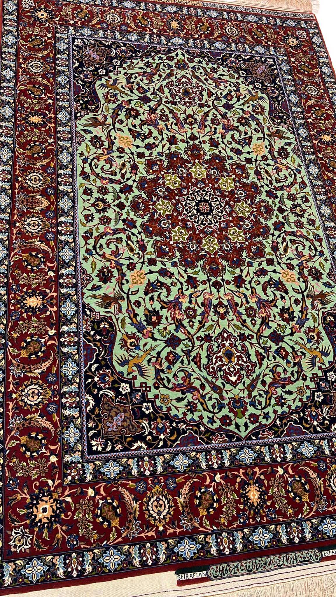 "Detailed view of a luxurious Seirafian Persian rug with silk and wool, featuring vibrant floral patterns on a light green background, hand-knotted in Isfahan."